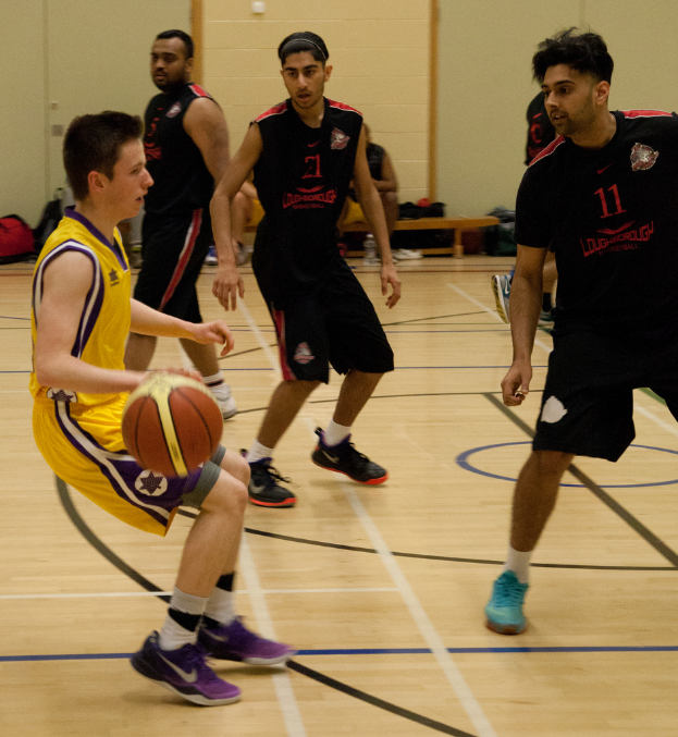 Menschen beim Ballspielen in einem Innenraum, einige sitzen auf einer Bank, und verschiedene Gegenstände wie Taschen, eine Platte und eine Flasche sind an einer Wand zu sehen.