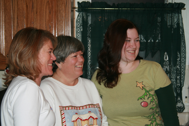 Frauen stehen lachend vor einer Wand mit grüner Gardine und einem hölzernen Fenster.