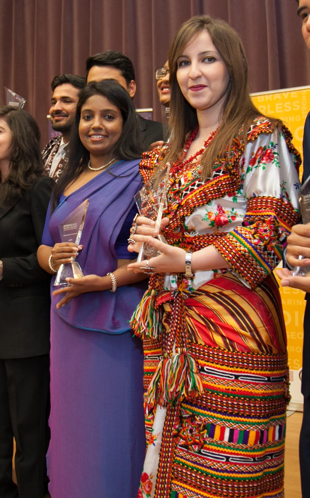 Eine Gruppe von Menschen auf einer Bühne mit einer Frau in der Mitte, die eine Trophäe hält, hinter einem Vorhang mit einer Tafel, auf der "Bravo Segenspreis-Gewinner" steht.