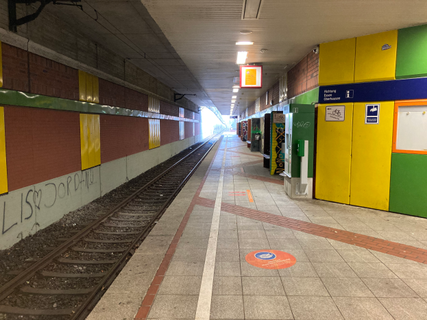 Ein Bahnhofsgebäude in Berlin, Deutschland, mit einem Zug auf den Gleisen, beleuchtet von Deckenlampen, Graffiti an der linken Wand und einigen Gegenständen auf der rechten Seite.