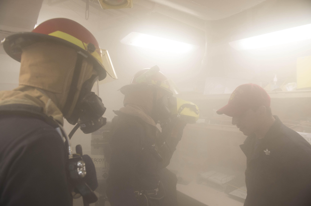 Feuerwehrleute in einem raucherfüllten Raum während einer Übung, einer hält eine Kamera.