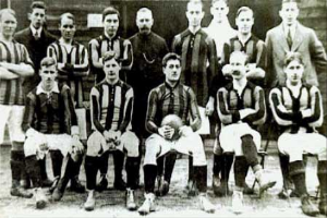 Ein Schwarz-Weiß-Foto einer Fußballmannschaft, einige stehen, andere sitzen, vor einer Wand, mit dem Text "Ballymena Football Club" unten.