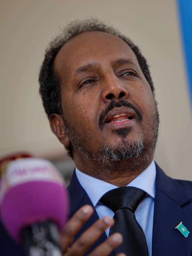 Ein Mann in Anzug und Krawatte spricht in ein Mikrofon auf einer formellen Veranstaltung.