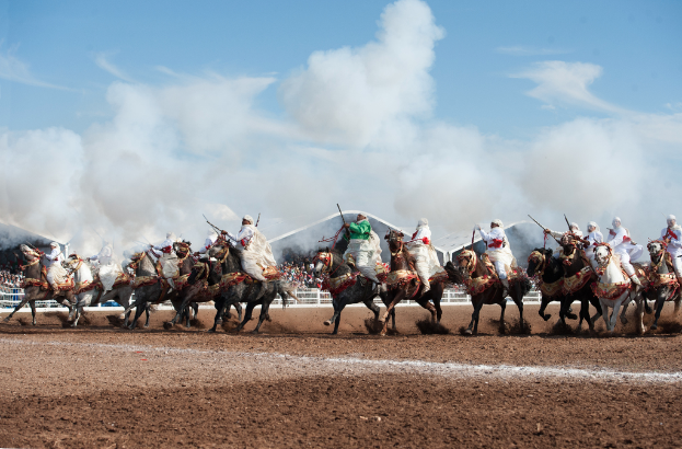 Menschen, die auf dem Boden reiten, mit anderen, Zäunen und Unterständen im Hintergrund bei einem bewölkten Himmel.