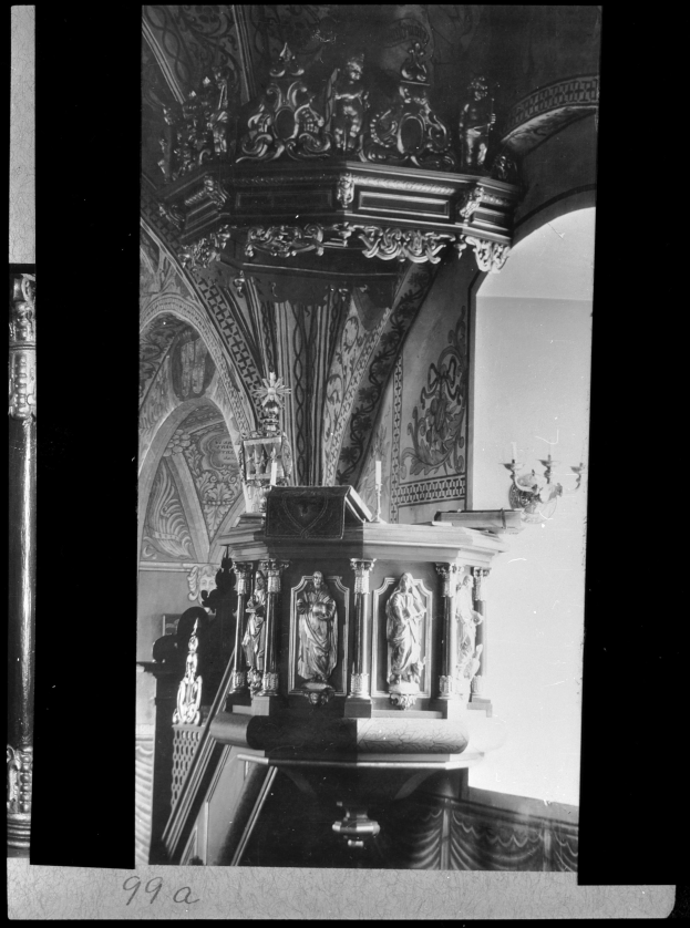 Ein Schwarz-Weiß-Foto eines Kirchenpults mit geschnitzten Säulen und einer texturierten Wand im Hintergrund, mit etwas Text unten.