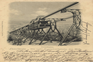 Ein altes Schwarz-Weiß-Foto einer Eisenbahnbrücke mit einem Kran, umgeben von Bäumen und einem bewölkten Himmel, mit Text unten, der lautet: "Bahnstrecka, die erste Eisenbahnbrücke in Deutschland".