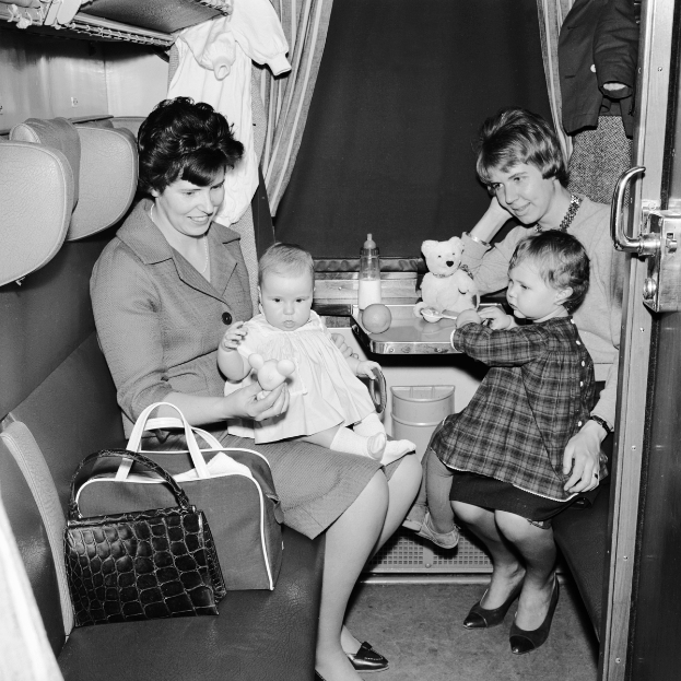 Ein Schwarz-Weiß-Foto von zwei Frauen und zwei Kindern, die in einem Zug sitzen, wobei eine Frau ein Baby hält und die andere zwei Kinder.
