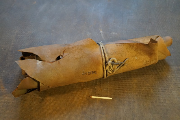 Ein brauner Papiertüte in Form einer Granate mit einem Griff oben drauf, mit einem Seil zugebunden und eine Zigarette daneben auf einem Tisch.