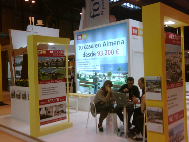 Ein Raum mit Menschen an einem Tisch, die auf Laptops arbeiten, umgeben von mehreren Flyern mit verschiedenen Anzeigen.