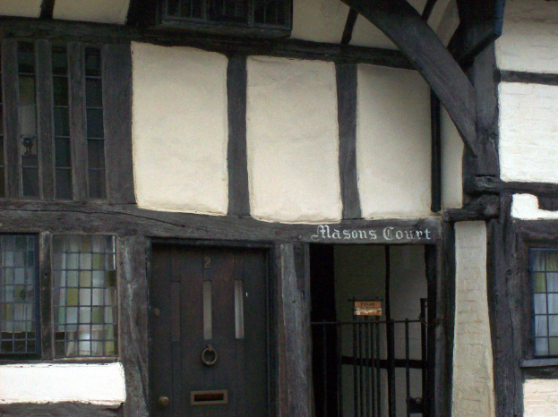 Ein Gebäude mit einer Tür im Vordergrund, einem Geländer, Fenstern mit Vorhängen auf beiden Seiten und Text an der Wand.