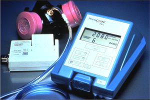 Eine Gasmask auf einem Tisch neben einem elektronischen Gasdetektorgerät mit einem angeschlossenen Kabel.