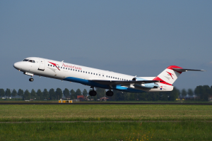 Austrian Airlines Embraer ERJ-190 Flugzeug startet am Frankfurter Flughafen, mit grünem Gras darunter und Bäumen und Gebäuden im Hintergrund.