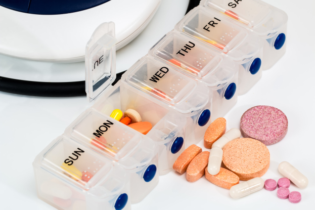 Weißer Tisch mit einem Pillenschächtelchen, das Pillen enthält, und einem Stethoskop daneben, Pillenschächtelchen mit Text beschriftet.