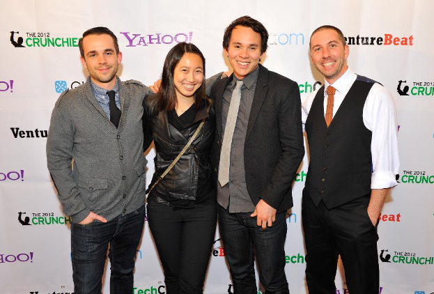 Eine Gruppe von strahlenden Menschen, die für die Kamera posieren, mit einem Sponsorenbanner im Hintergrund.