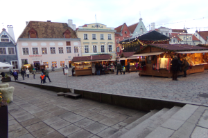 Ein geschäftiges Weihnachtsmarkt in Tallinn, Estland mit Menschen um dekorierte Stände, festliche Lichter, Topfpflanzen, Treppe nach oben und bewölktem Himmel.