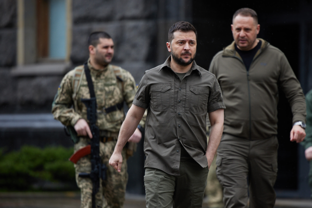 Ein Mann in militärischer Uniform, bei dem es sich mutmaßlich um den ehemaligen ukrainischen Präsidenten Viktor Janukowytsch handelt, wird von zwei bewaffneten Männern in militärischer Uniform vor einem Gebäude mit Pflanzen im Hintergrund eskortiert.