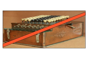 Eine alte Kasse mit einem roten Kreuzsymbol oben drauf, mit Tasten und einem roten Band, auf einem Tisch.