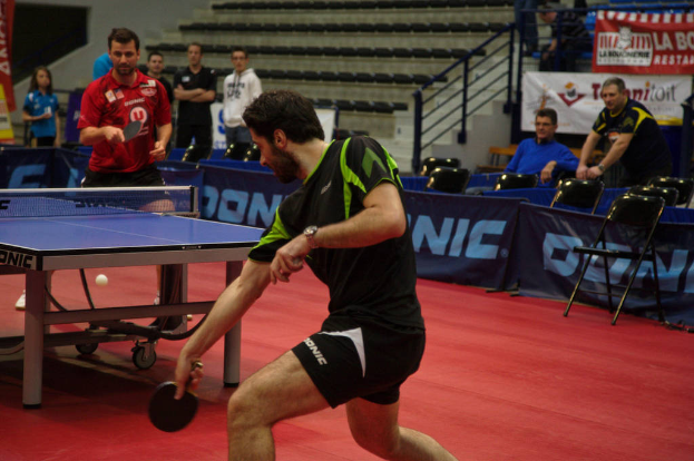 Eine Gruppe von Menschen in verschiedenen Farben, darunter schwarz, weiß und blau, sitzt um einen Tisch mit einem Spiel im Gange, mit Stühlen, einer Treppe und einem Ball im Hintergrund.