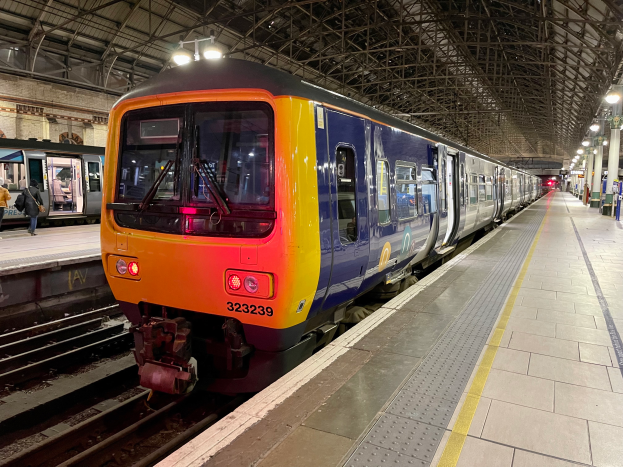 Ein Zug fährt auf einem Bahnsteig ein, mit Menschen, die gehen, einer Handtasche im Zug und Deckenleuchten im Bahnhof.