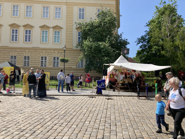 Eine Gruppe von Menschen geht eine Kopfsteinpflasterstraße in Krakau, Polen, entlang mit Zelten, Tischen mit Gegenständen und einem Gebäude mit sichtbarem Text im Hintergrund.