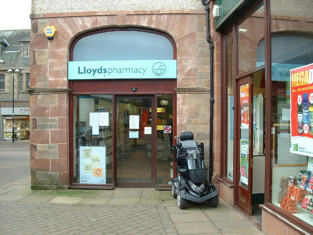 Eine Apotheke mit einem vor ihr geparkten Auto und einem Gebäude in der linken Ecke.