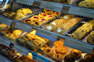 Ein Bäckereivitrinenregal voller verschiedener Gebäcke, darunter Kuchen und Plätzchen, mit Schildern, die die Art der Backwaren angeben.