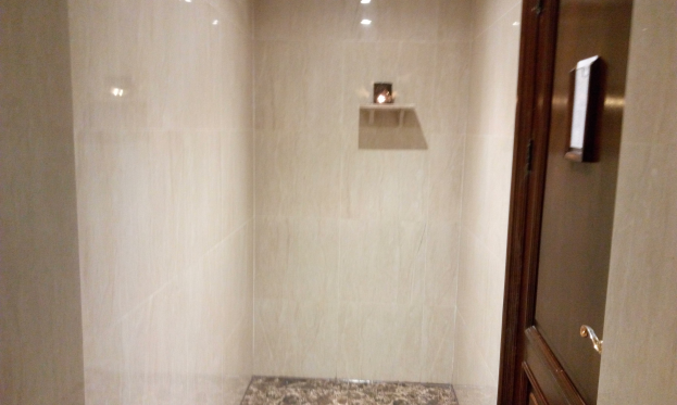 Badezimmer mit einer Duschkabine, Toilette und gefliesten Wänden, mit Deckenleuchten und einer Tür auf der rechten Seite.