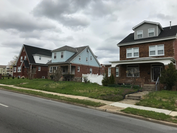 Eine Reihe von Häusern in der Renovierung mit verstreuten Werkzeugen und Materialien, mit Fenstern, Türen, Stufen, Geländern, Pflanzen, Gras, Bäumen und einem bewölkten Himmel.