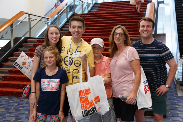 Eine Gruppe von Menschen, die vor einer Rolltreppe stehen, lächeln und Taschen halten.