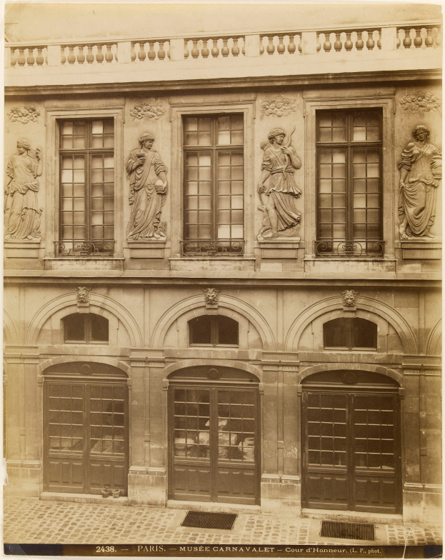 Ein altes Gebäude mit Fenstern, Türen und Skulpturen an seiner Fassade, mit Text am unteren Bildrand.