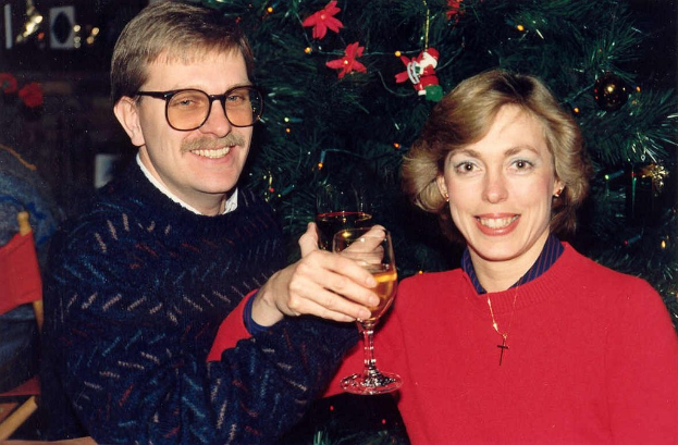 Ein Paar lächelt bei einem Glas Wein, mit einem Weihnachtsbaum im Hintergrund.