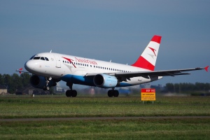 Austrian Airlines Airbus A320-200 startet von Frankfurt Airport mit einer Tafel im Vordergrund, Gras, Bäumen, Gebäuden und einem klaren blauen Himmel.