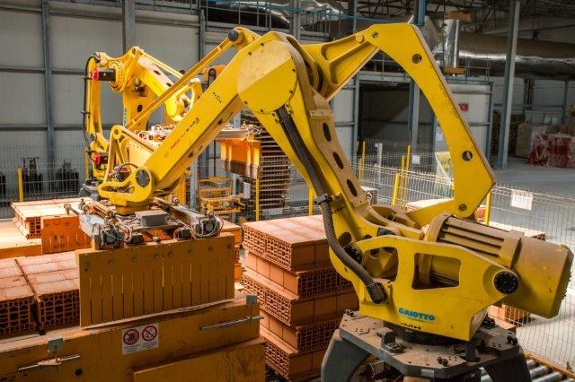 Großes Industriegebäude mit gestapelten Kisten, Kränen an der Decke, Zaun, Pfosten und einer fernen Wand in einer automatisierten Fertigungsumgebung.