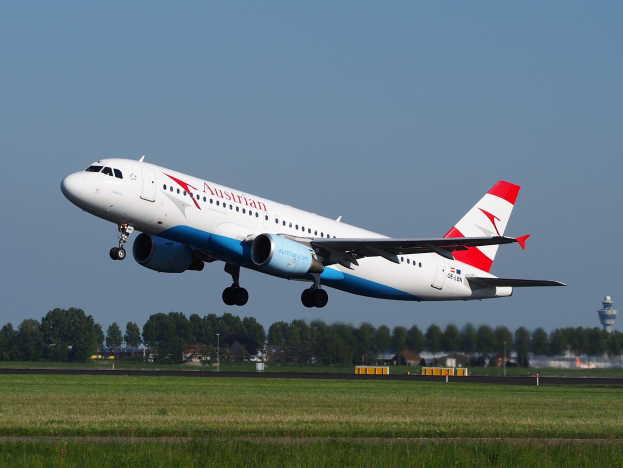 Airbus A320-200 der Austrian Airlines startet vom Frankfurter Flughafen mit grünem Gras darunter, Bäumen und Gebäuden im Hintergrund und einem Tower auf der rechten Seite.