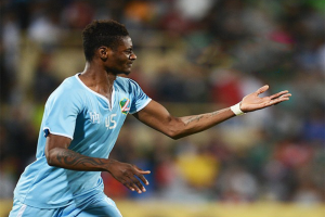 Ein Fussballspieler in einem blauen Trikot feiert mit ausgestreckten Armen nach einem Torerfolg, mit einem unscharfen Hintergrund.