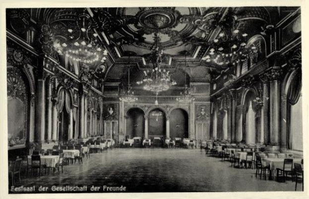 Schwarzes und weißes Foto einer großen Halle mit Tischen, Stühlen, Säulen, Bögen und Deckenleuchter, beschriftet mit 'Festival der Gesellschaft der Freunde, Berlin' unten.