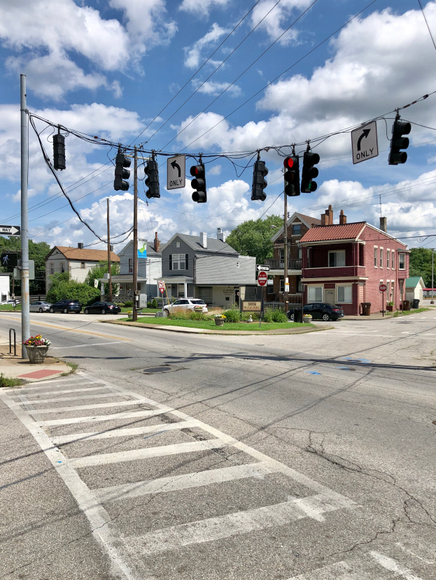 Eine Stadtstraße mit einer Ampel, Verkehrszeichen, Fahrzeugen, Strommasten, Schildern, Gebäuden mit Fenstern, Bäumen und einer bewölkten Himmel.
