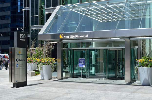 Moderner Glasbau der Sun Life Financial in Toronto mit einem Schild, Topfpflanzen mit Blüten, Menschen, einer Straßenlaterne, einem Schild, Fahrzeugen auf der Straße und einem bewölkten Himmel.