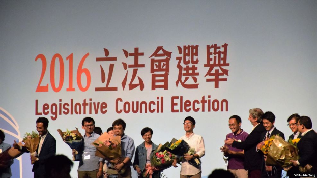 Eine Gruppe von Menschen auf einer Bühne mit Blumensträußen in den Händen, mit einem Publikum darunter und einem Bildschirm mit Text und Logo für die Wahl zum Landtag 2016 im Hintergrund.