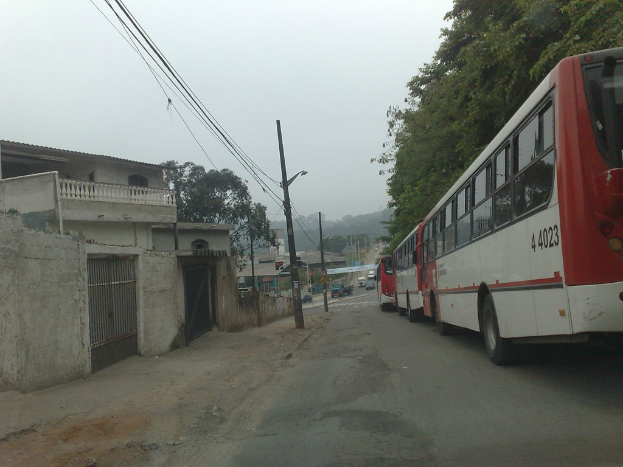 Eine mostly leere Straße mit wenigen Fahrzeugen in der rechten Ecke, Gebäuden, Polen und Drähten in der linken Ecke und Bäumen im Hintergrund.