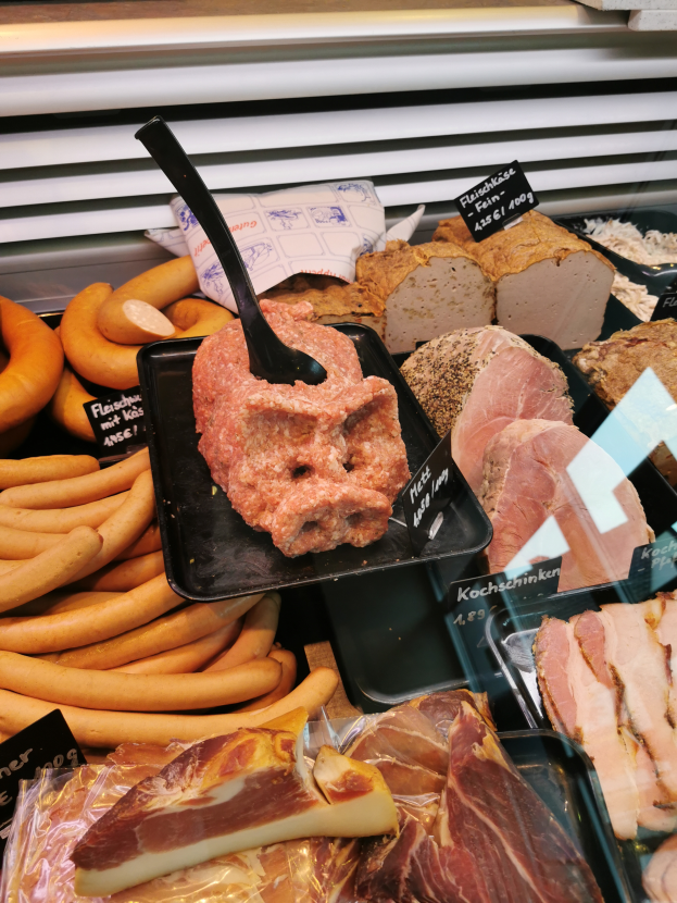 Eine Vitrine voller verschiedener Fleisch- und Wurstsorten, mit einer schwarzen Platte in der Mitte, die ein Stück Fleisch und einen schwarzen Spatel trägt.