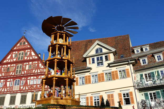 Ein festlicher Weihnachtsmarkt in Rothenburg ob der Tauber, Deutschland, mit einem hölzernen Aufbau mit Windmühle, umgeben von Menschen, Pflanzen und anderen Gegenständen, unter einem sichtbaren Himmel.